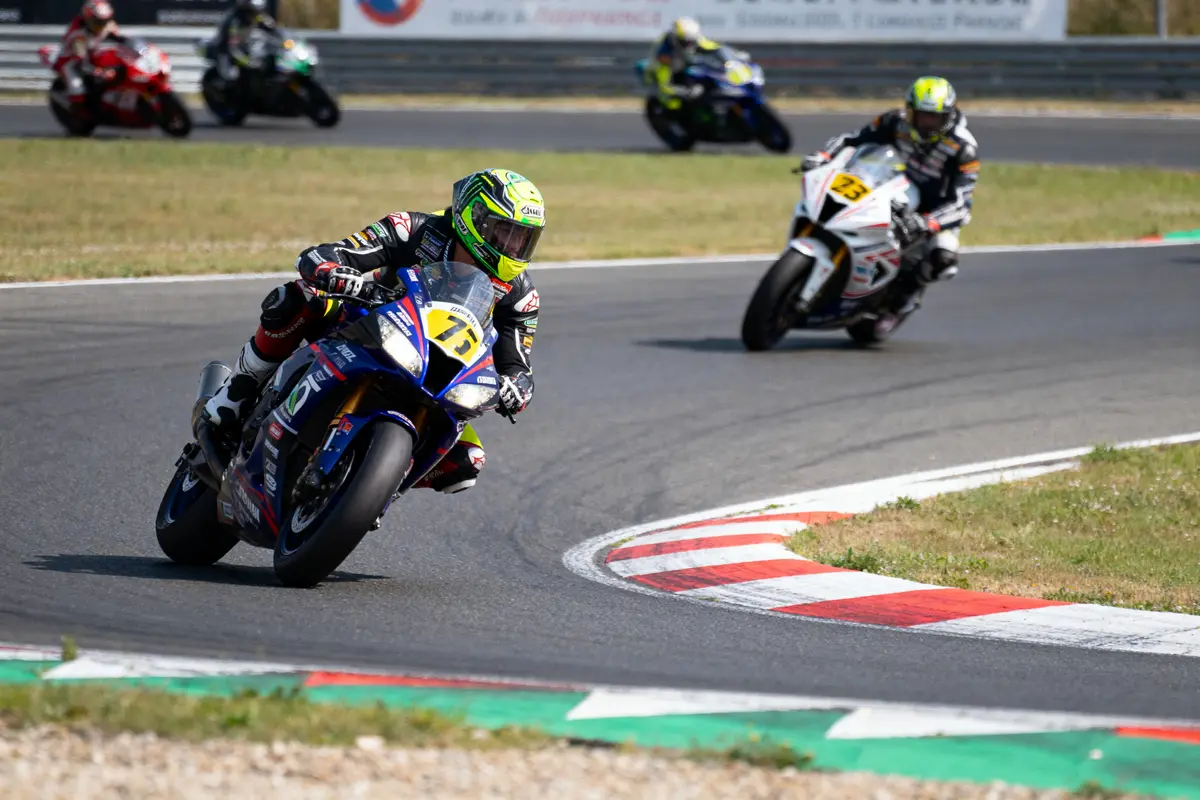 Motards en course sur circuit, virage serré, casques et combinaisons colorées, journée ensoleillée, mécanisme précis, compétition intense.