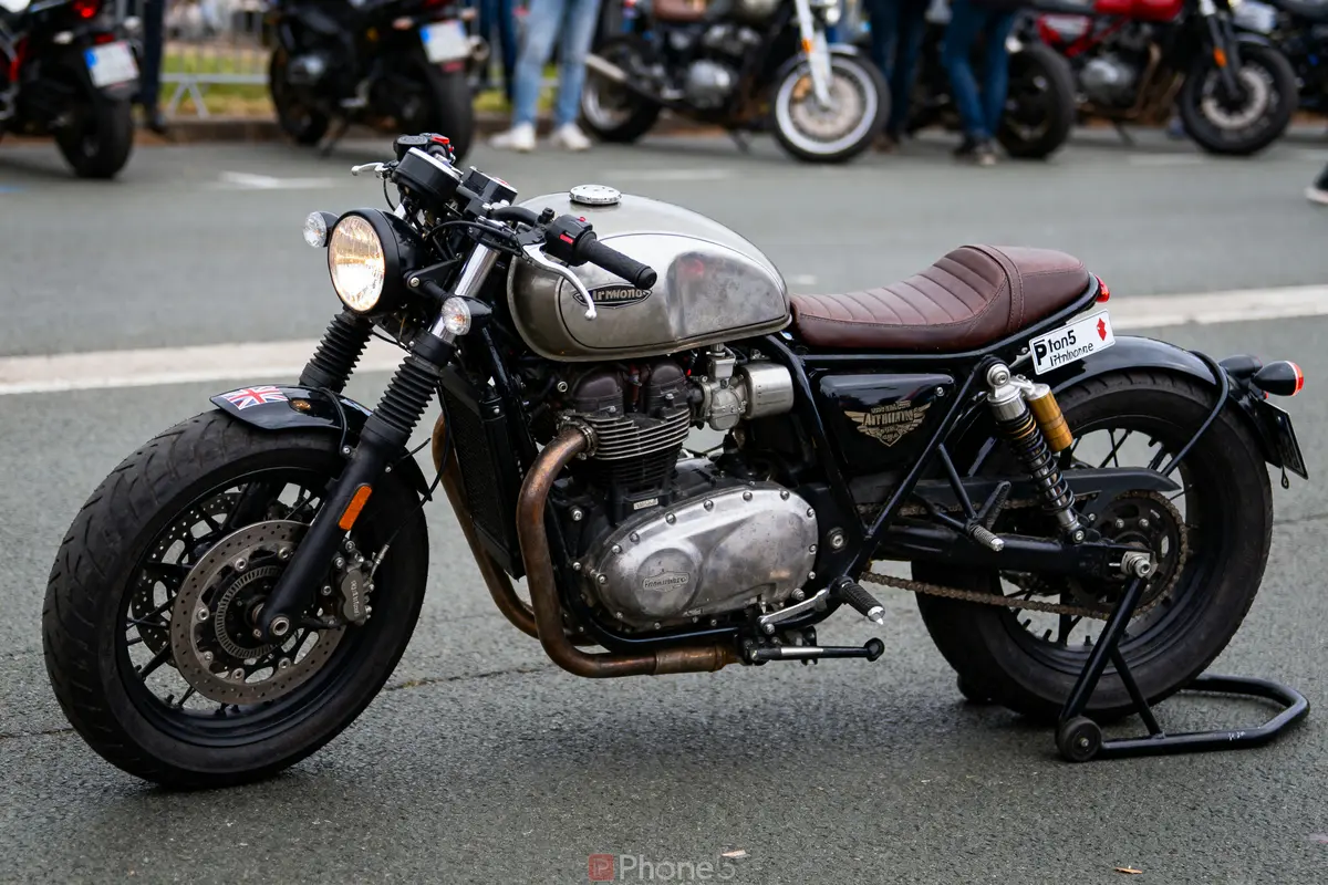 Moto vintage rétro stationnée sur une route, avec détails en métal brut et siège en cuir marron.