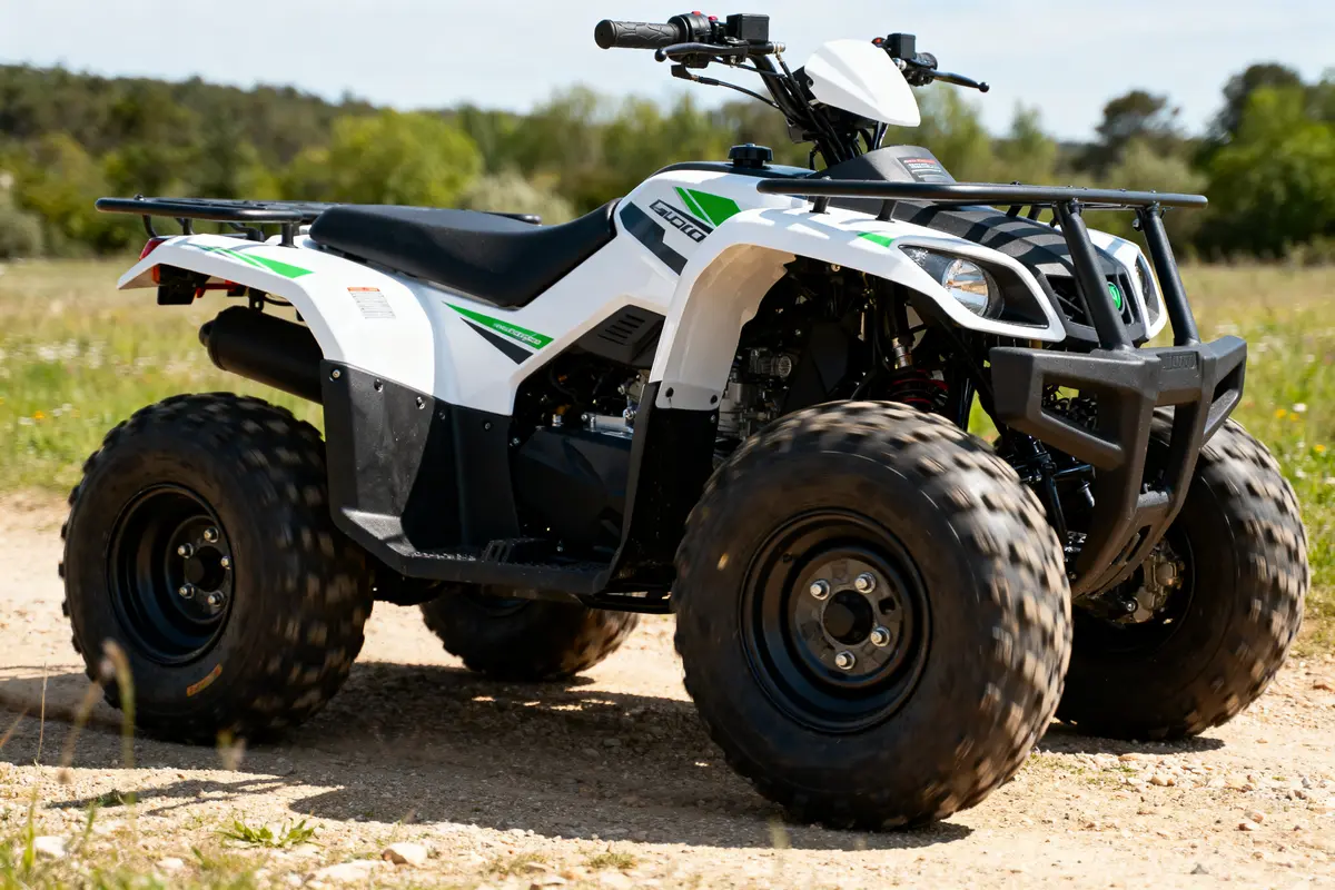 Quad blanc et vert sur chemin de terre avec fond de végétation et ciel dégagé.