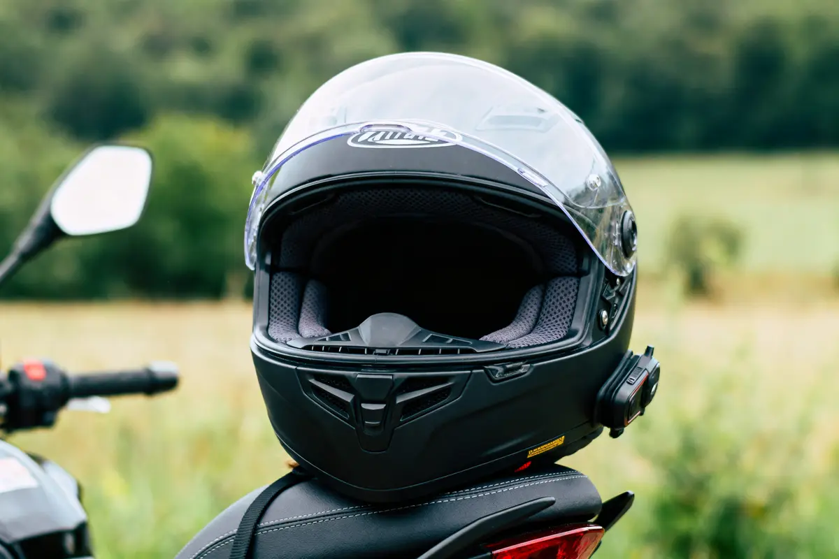 Casque de moto noir avec visière transparente, posé sur une selle, arrière-plan flou de nature verdoyante.