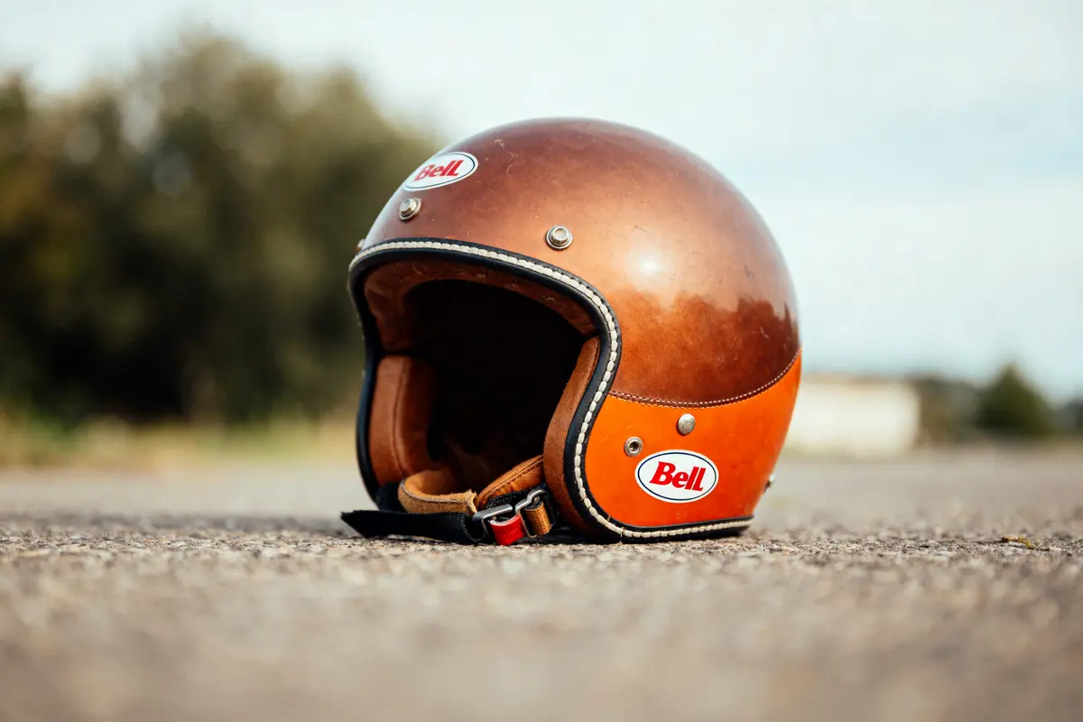 Casque rétro Bell marron posé sur le sol, arrière-plan flou.