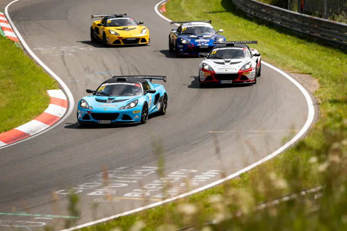 Quatre voitures de sport en course sur circuit sinueux, tournant à gauche, temps ensoleillé.