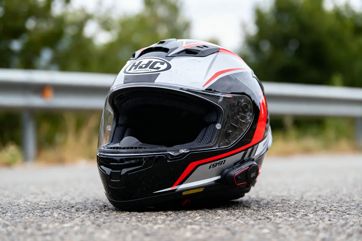 Casque de moto HJC noir et rouge posé sur la route, barrière de sécurité en arrière-plan.