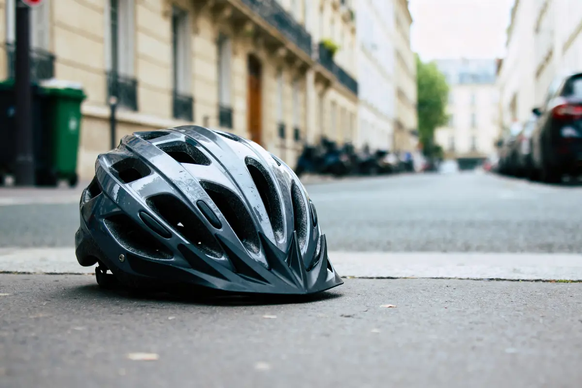 Casque de vélo noir au sol, rue urbaine floue en arrière-plan.