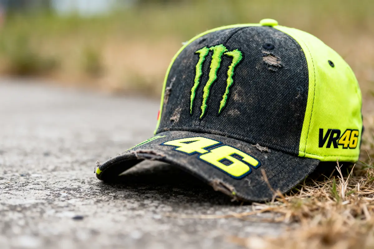 Casquette usée sur le sol avec logos Monster et VR46, fond naturel flou.