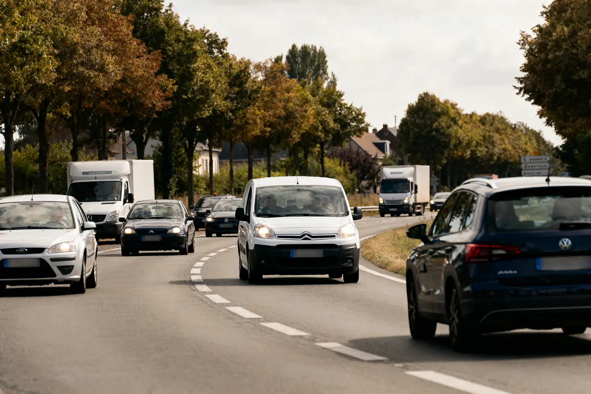 Route bordée d'arbres avec circulation de voitures et camions par temps clair.