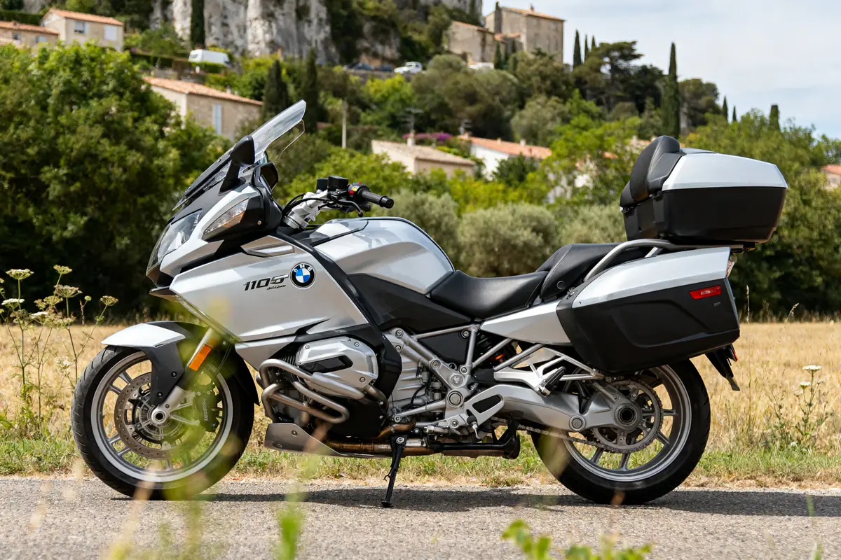 Moto BMW K 1200 RT blanche garée sur route devant paysage rural verdoyant