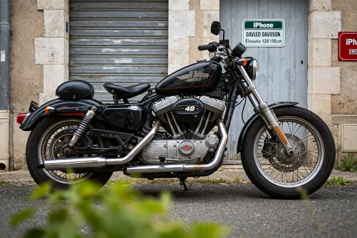 Moto vintage Harley-Davidson 48 stationnée devant une porte métallique dans une ruelle calme