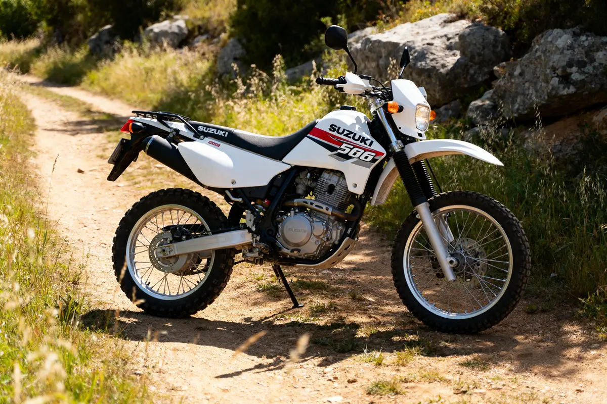 Moto Suzuki DR 650 blanche garée sur un chemin rural ensoleillé