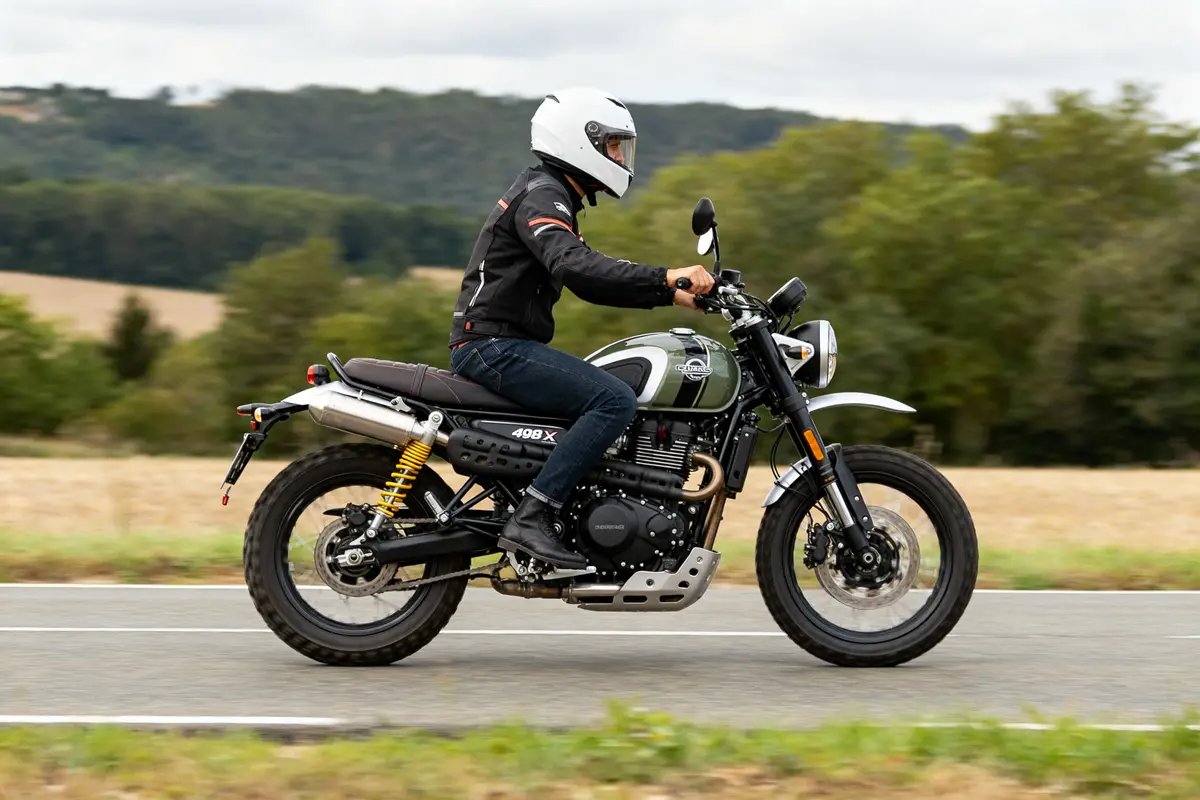 Motard roulant sur une scrambler 400 x verte sur une route de campagne boisée