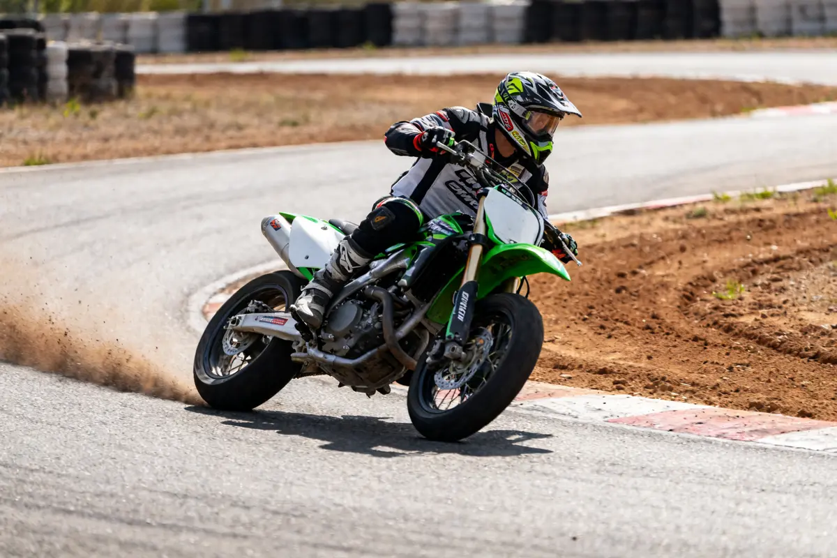 Pilote en supermotard supermoto accélérant dans un virage sur circuit poussiéreux.