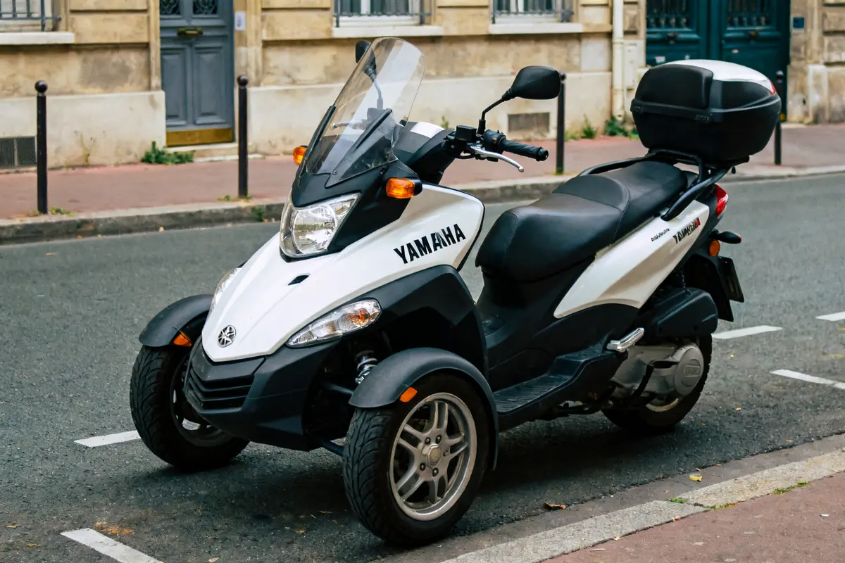 Scooter Yamaha 3 roues blanc stationné en ville sur une route pavée