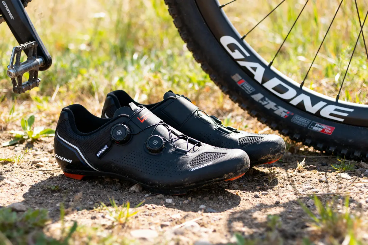 Chaussures de cyclisme Gaerne noires posées à côté d'une roue de vélo sur sol herbeux