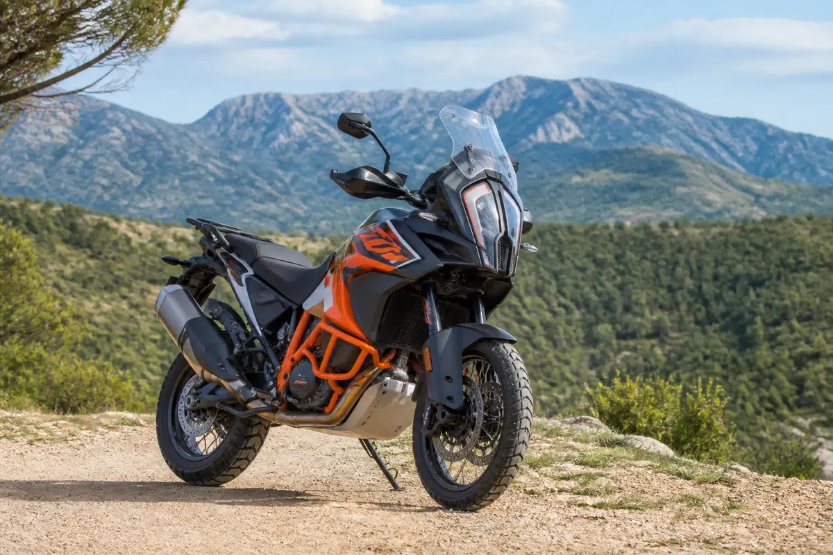 Moto KTM sur chemin de terre avec montagnes en arrière-plan sous un ciel bleu.