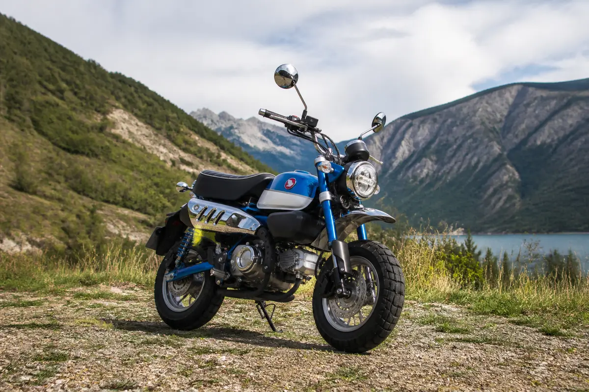 Moto bleue sur fond de montagnes et lac, ciel partiellement couvert. Atmosphère paisible et nature sereine.